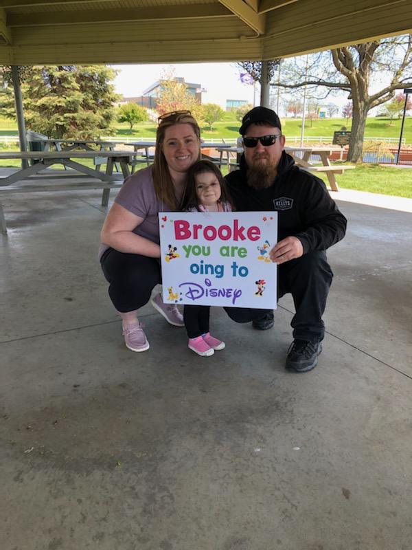 Brooke and parents with Going to Disney sign
